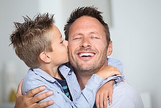 Ein Vater wird von seinem Sohn auf die Wange geküsst.